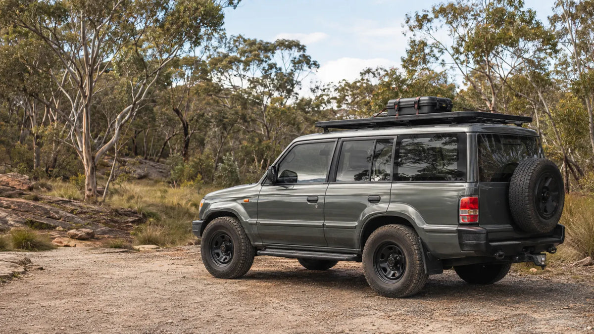 Generic boxy 4WD with a low-profile roof rack and restrained cargo at an Australian bush trailhead