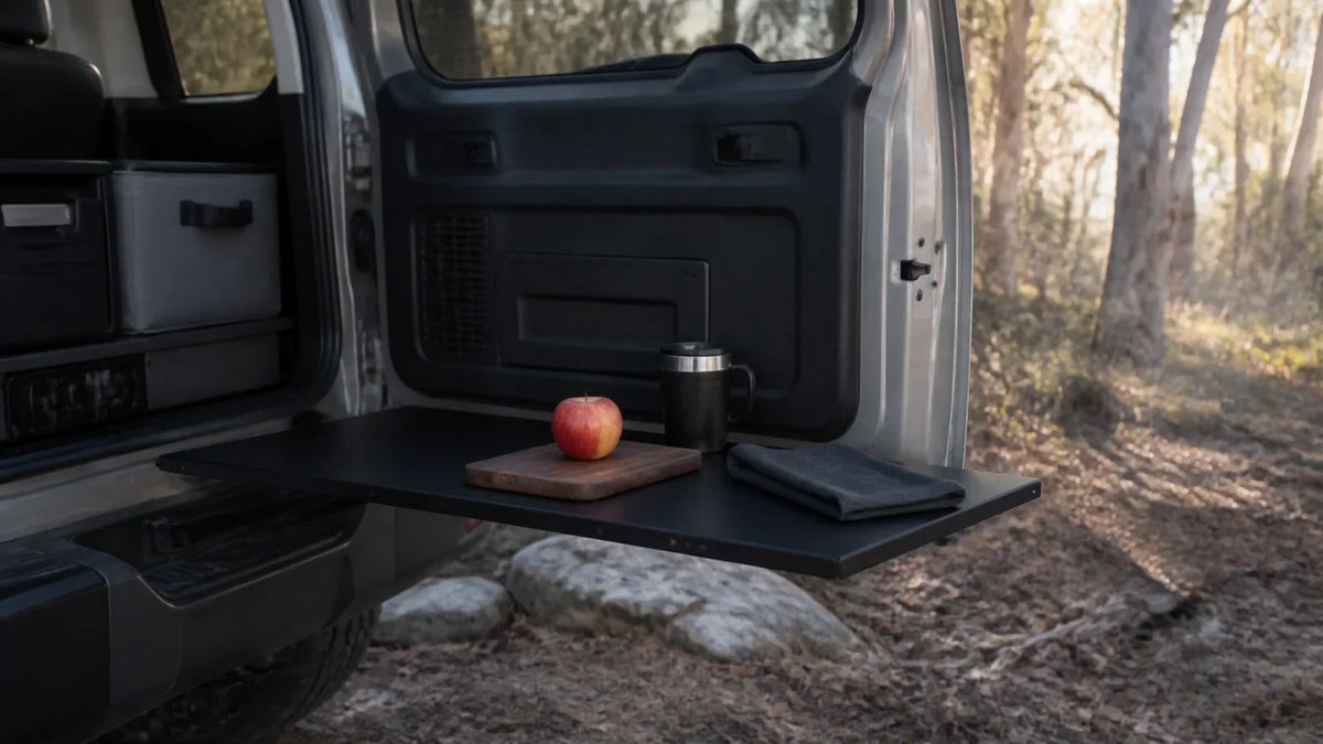 Conceptual campsite food-preparation surface on an open rear door, with an apple and covered cup